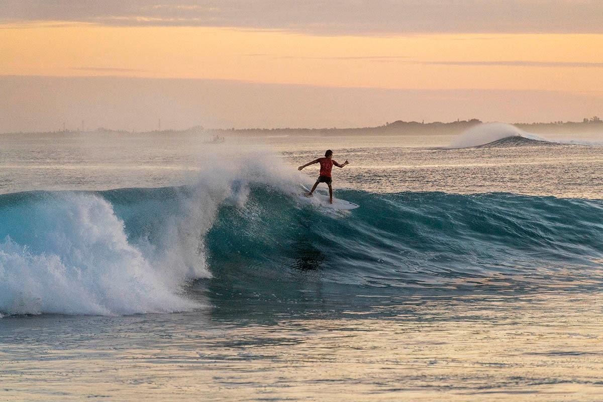 A surfer riding a glassy Maldivian reef break at golden hour, island silhouette on the horizon